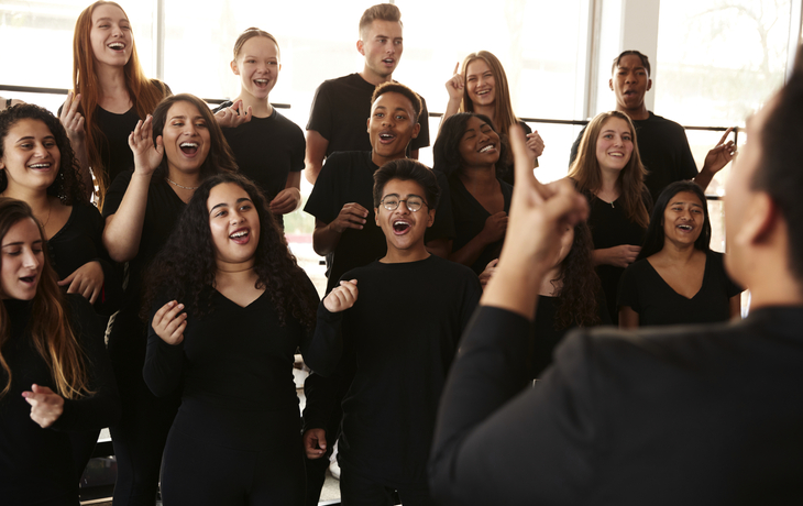 Männliche und weibliche Studenten, die im Chor mit Lehrer At Performing Arts School singen