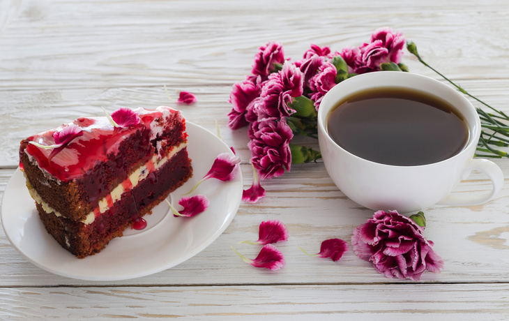 Roter Samtkuchen,Tasse Kaffee und rosa Nelken auf Holztisch